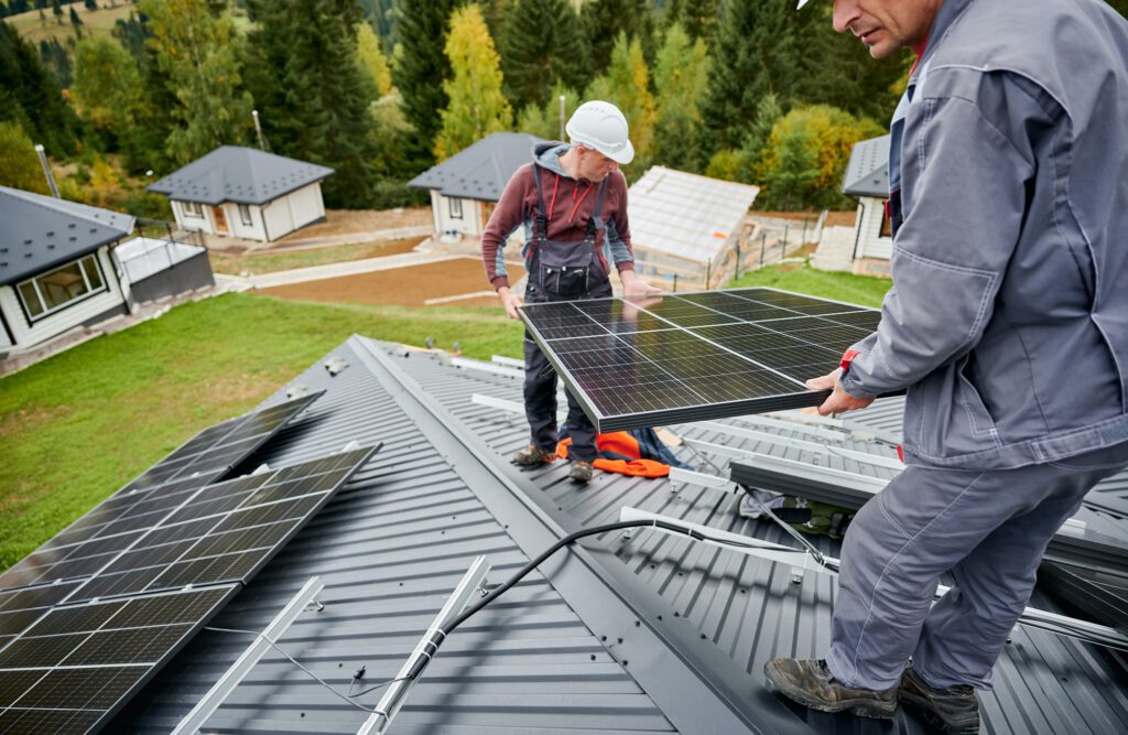 Technicians carrying photovoltaic solar module while installing solar panel system on roof of house